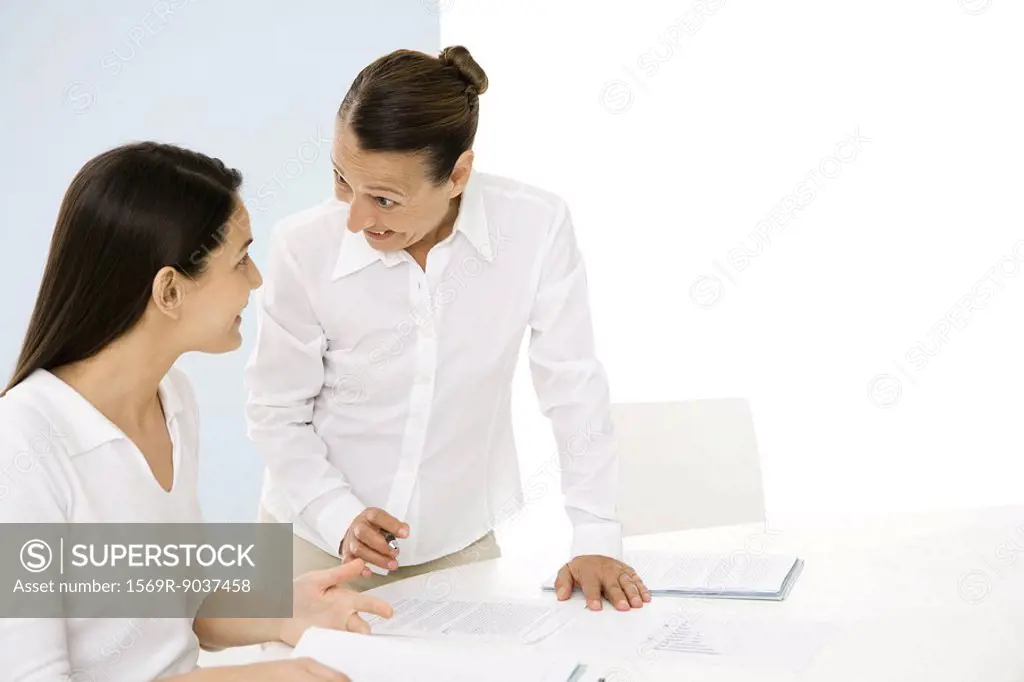 Two professional women discussing documents, smiling at each other