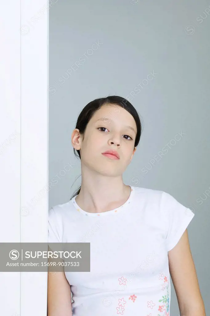 Preteen girl leaning against doorway, looking at camera