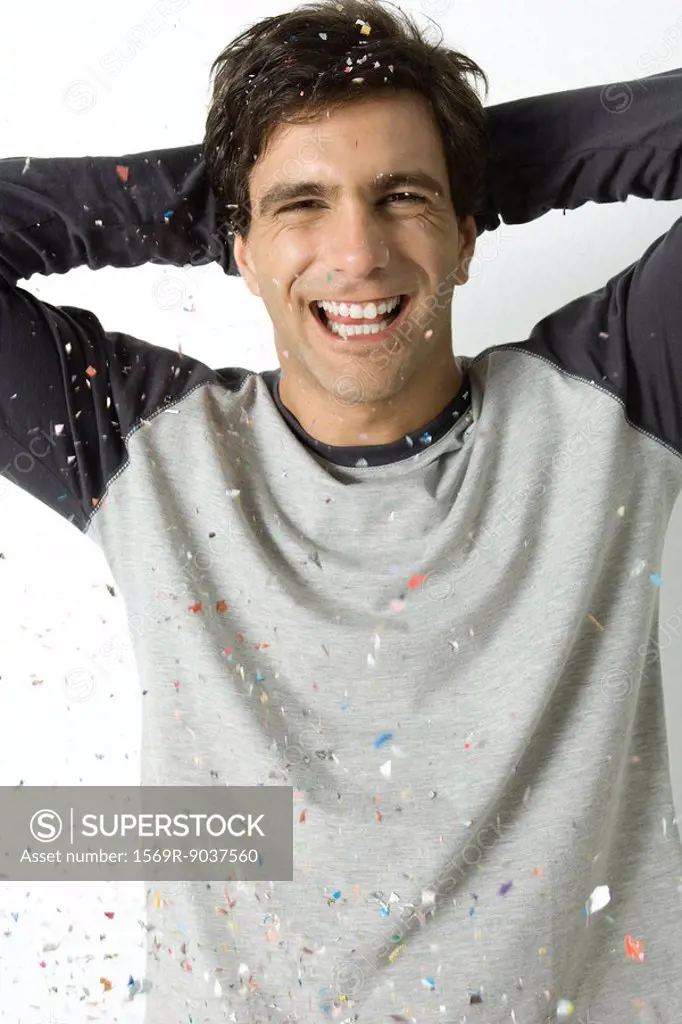 Young man amidst falling confetti, laughing at camera, hands behind head