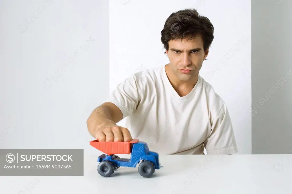 Man playing with toy dump truck, looking at camera with furrowed brow