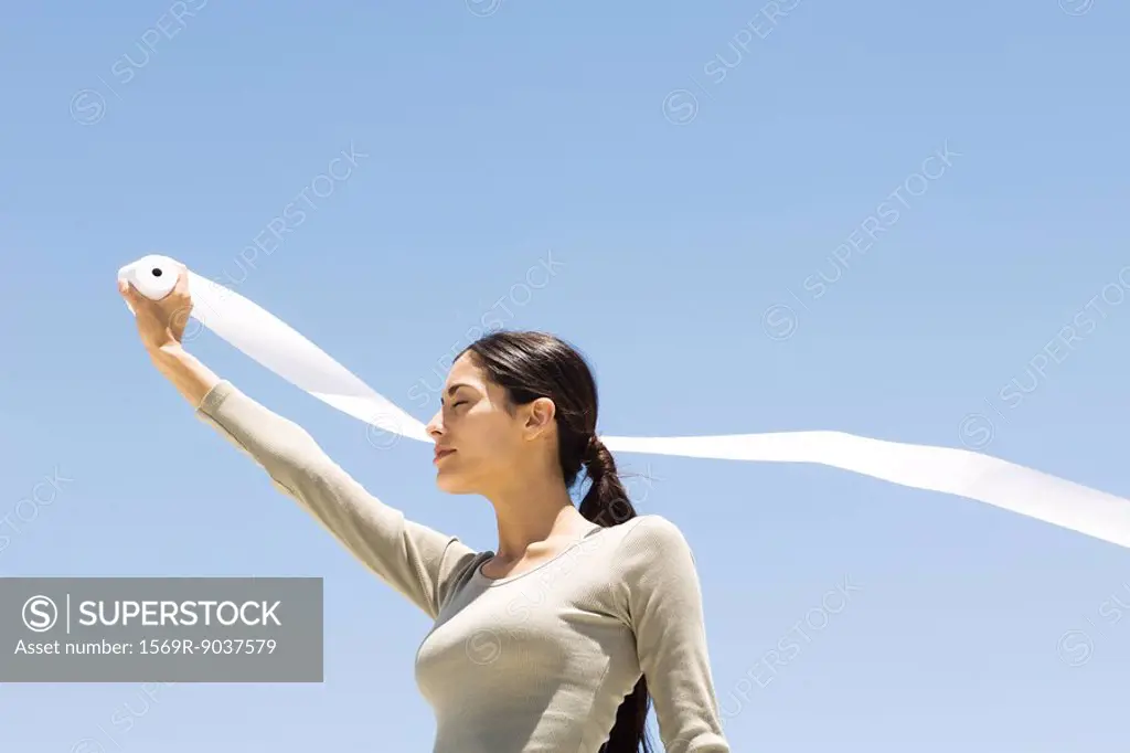 Woman holding up roll of paper outdoors, eyes closed, low angle view