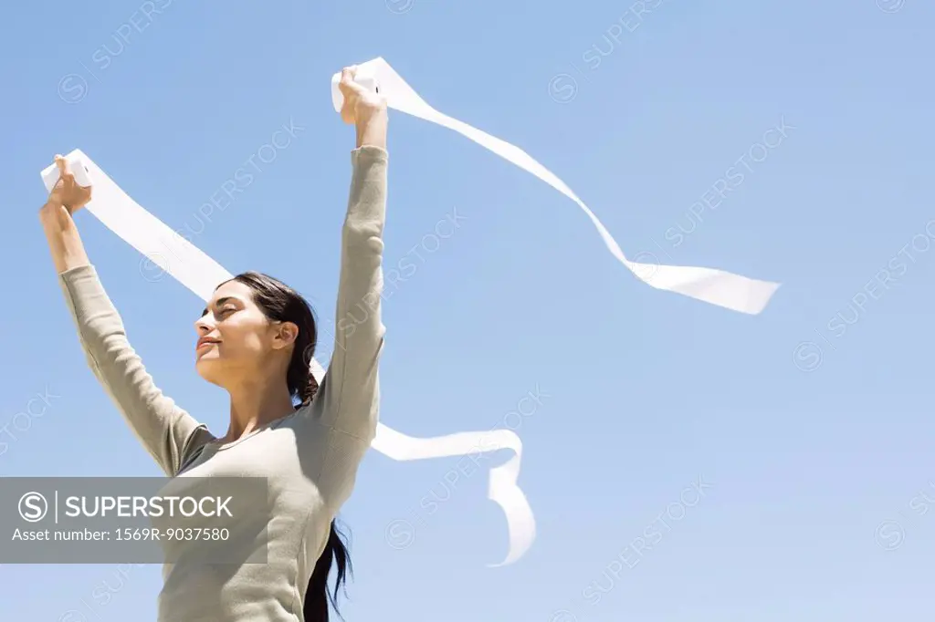 Woman holding up rolls of paper outdoors, eyes closed, low angle view