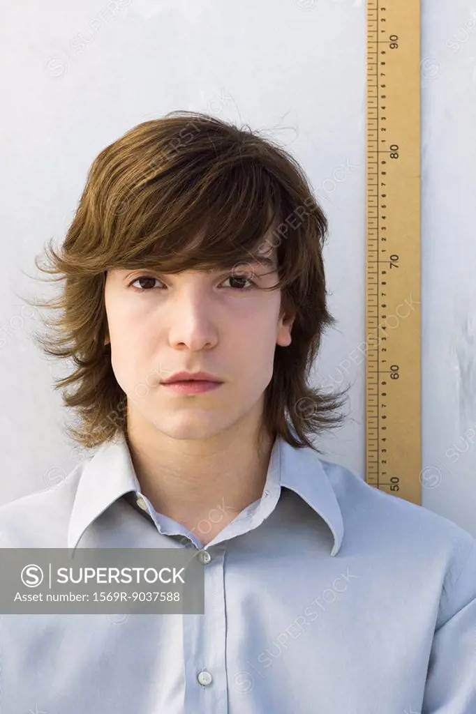 Young man standing in front of ruler, looking at camera