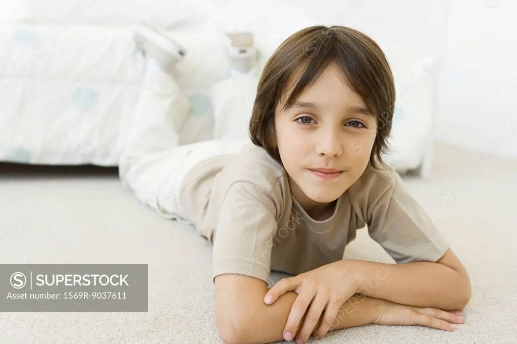 Boy lying on the floor in bedroom, smiling at camera
