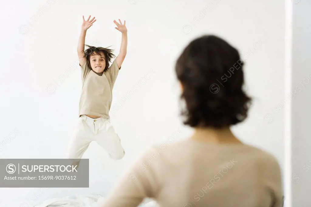 Boy jumping on bed, mother watching from doorway