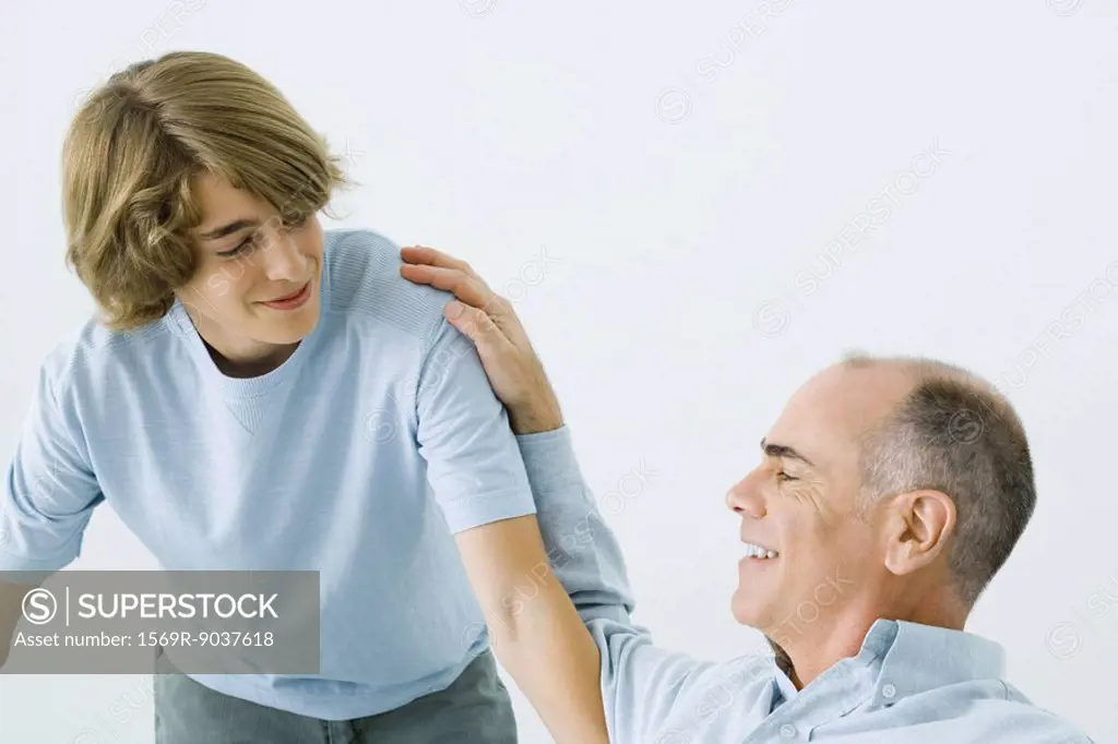 Man sitting with hand on teen son´s shoulder, both smiling