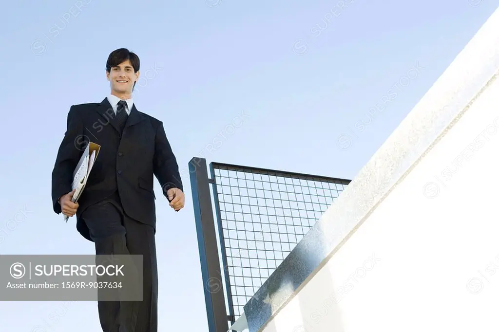 Businessman walking outdoors, carrying folder, low angle view