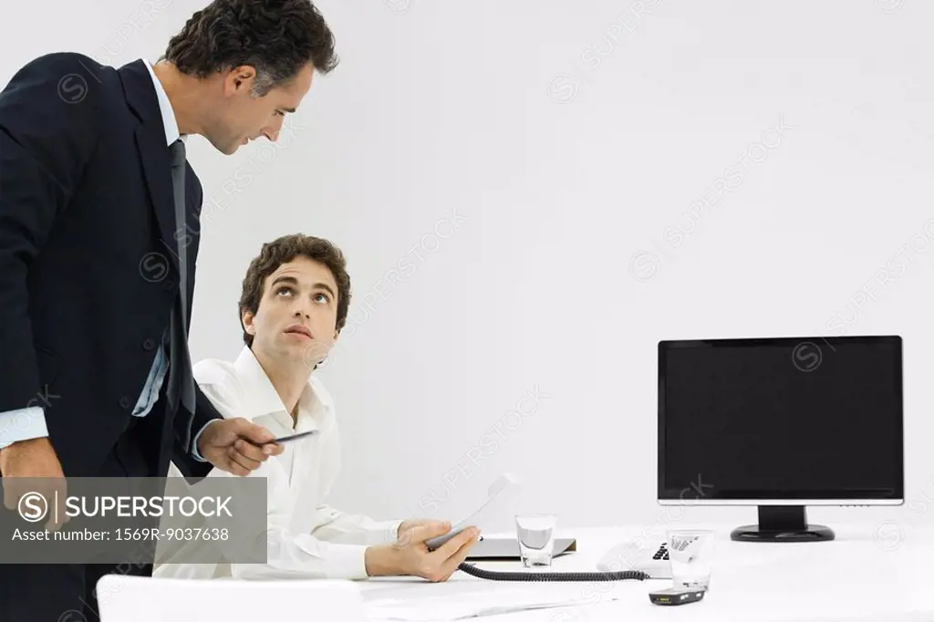 Professional man at desk holding phone, looking up at manager standing beside him