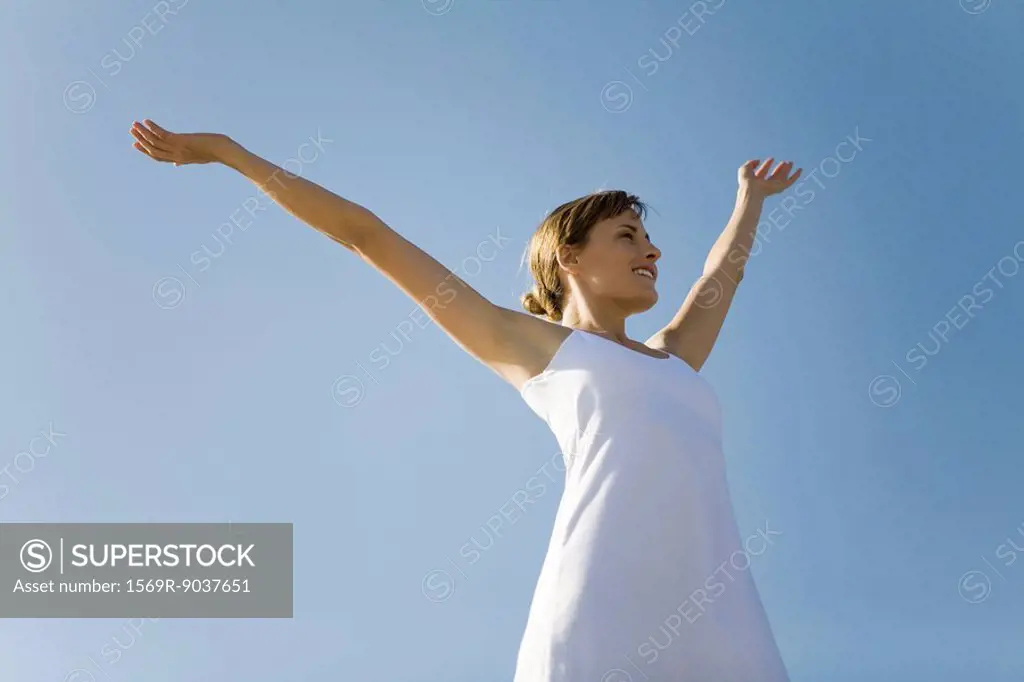 Woman standing outdoors with arms raised, smiling, low angle view