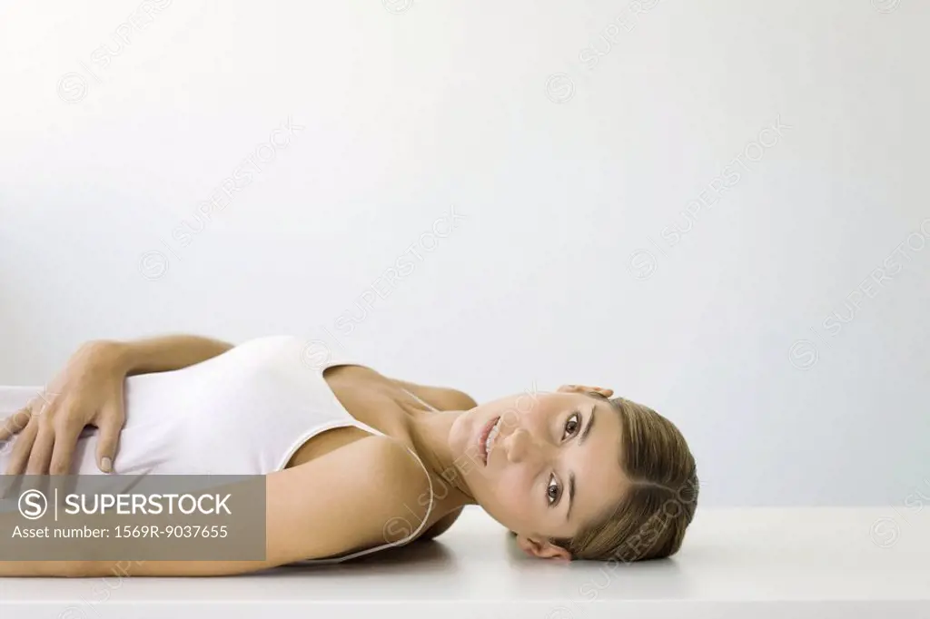 Woman lying on back, hand on stomach, looking at camera