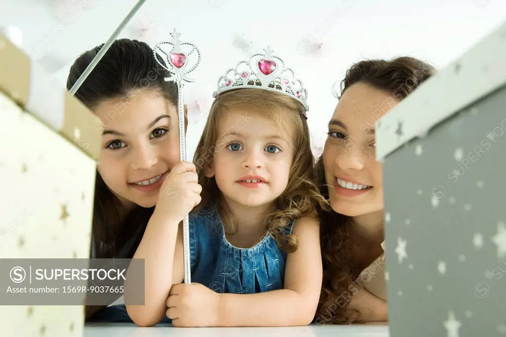 Little girl with mother and sister, dressed as princess, birthday gifts in foreground