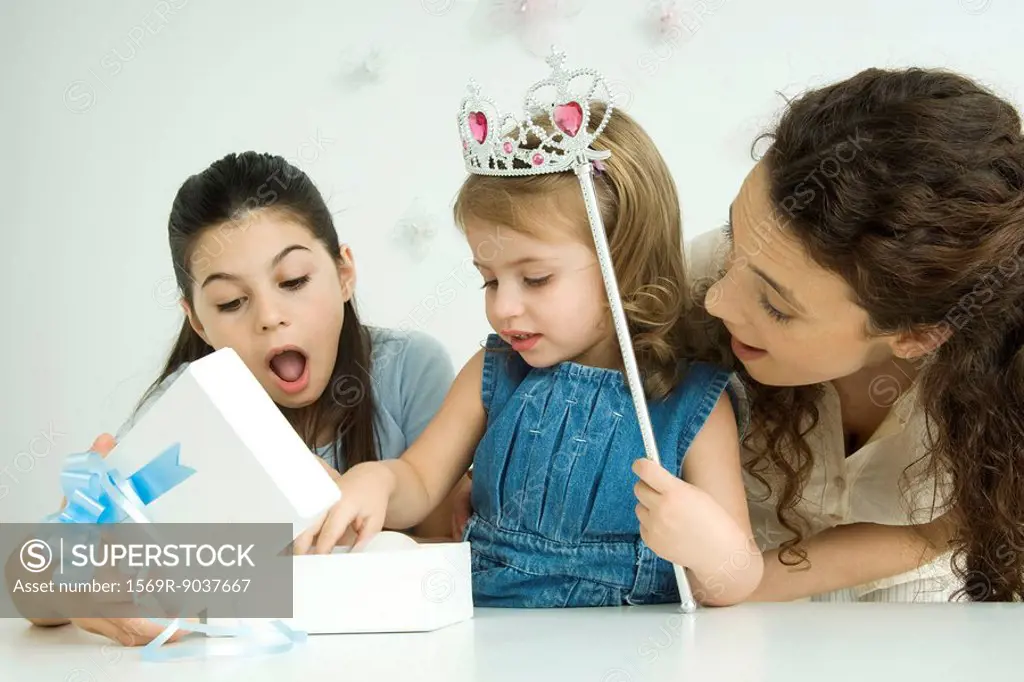 Little girl opening birthday present, mother and sister watching