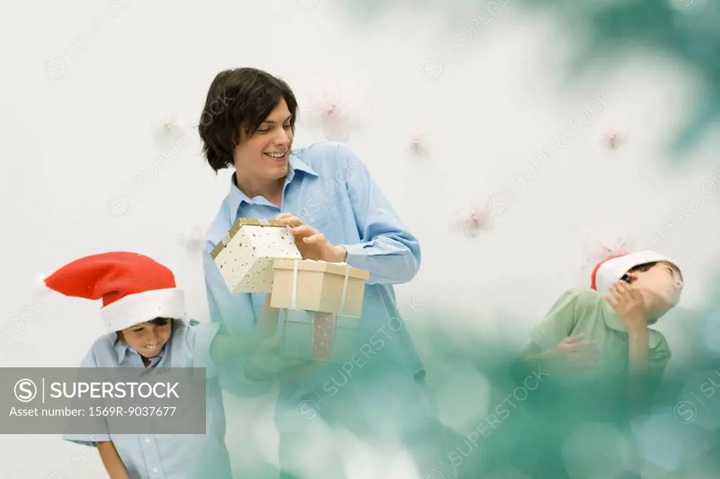Young man with presents, playing with two boys wearing Santa hats