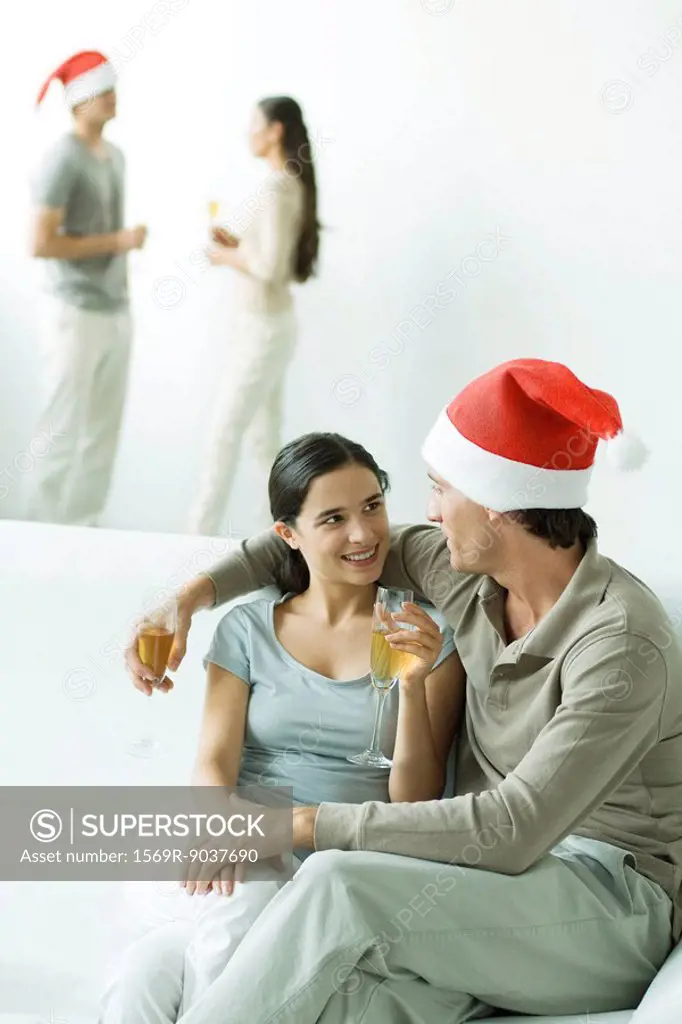 Couple at Christmas party, sitting together on sofa, champagne glasses in hands