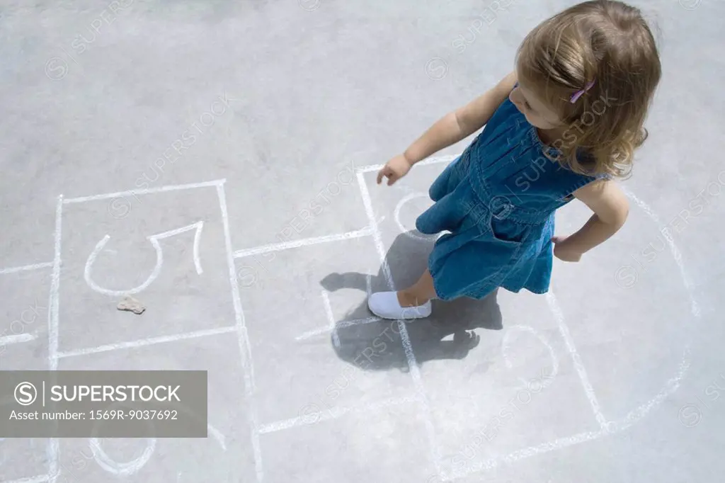 Little girl playing hopscotch outdoors, overhead view