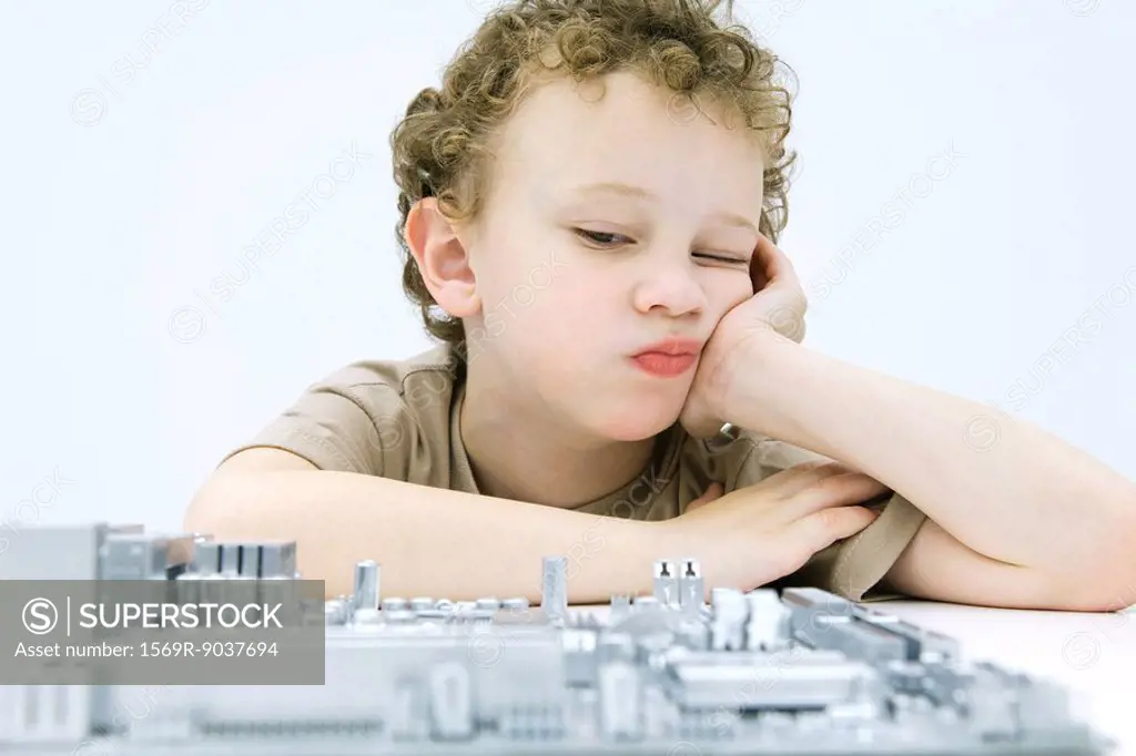 Little boy leaning on elbow, contemplating computer motherboard