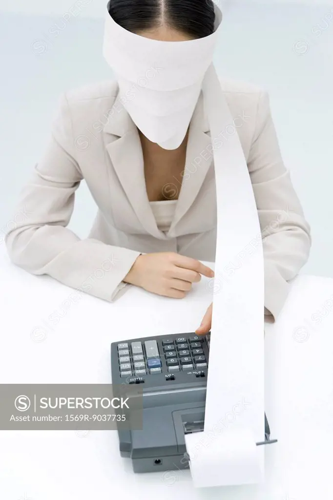 Businesswoman using adding machine, blindfolded with paper printout