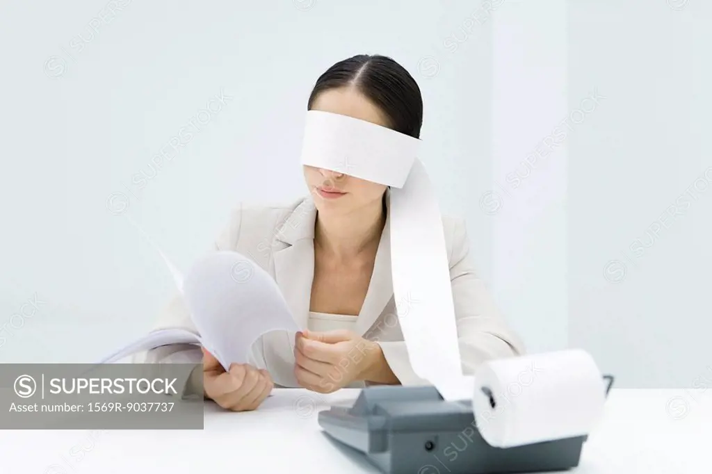 Female accountant blindfolded with paper from adding machine, holding document