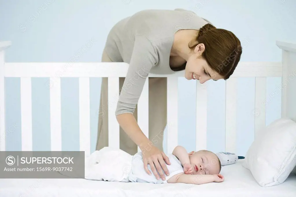 Mother leaning over side of crib to check sleeping infant
