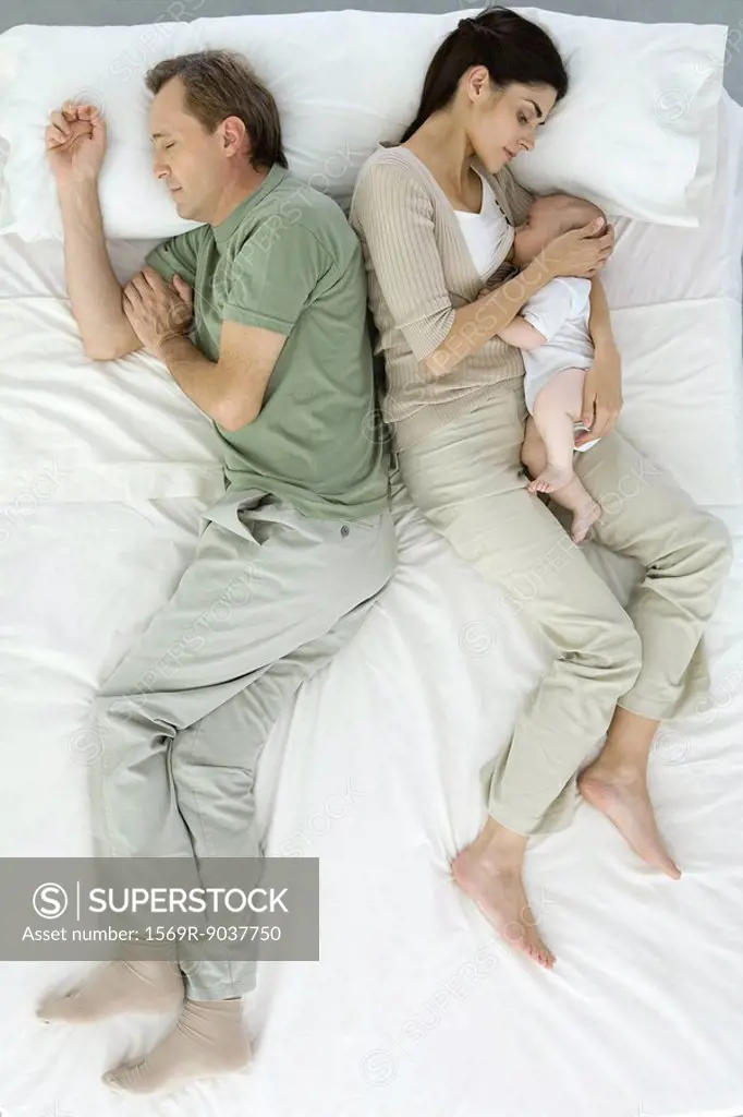 Family resting on bed, mother nursing baby, overhead view