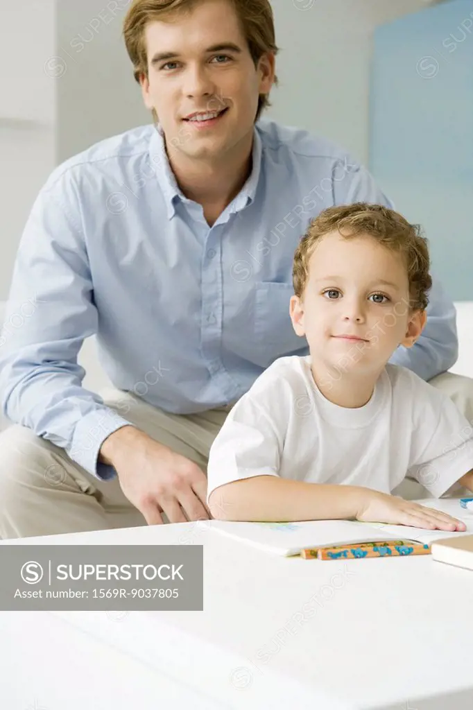 Father and son sitting together with book, both smiling at camera
