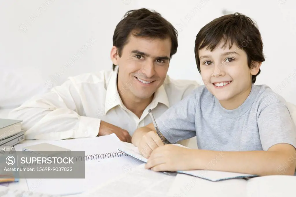 Boy doing homework with father, both smiling at camera