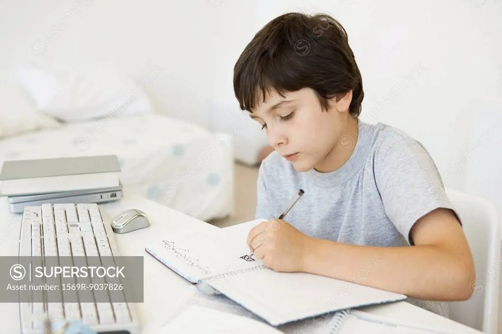 Boy sitting at desk in bedroom, doodling in notebook