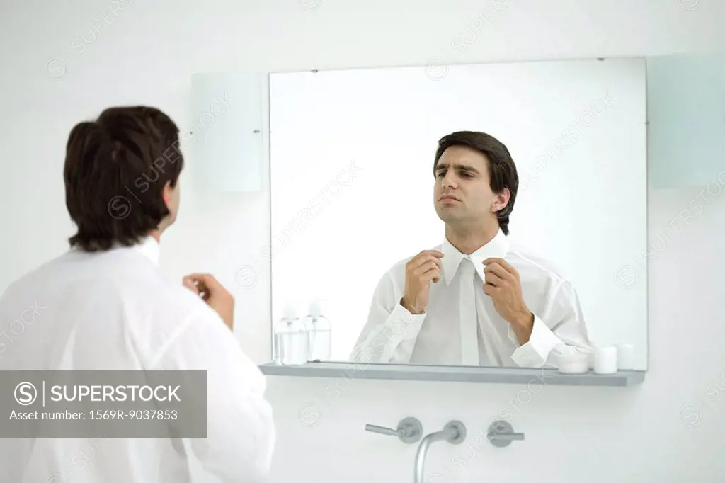 Man wearing button down shirt, adjusting collar in mirror