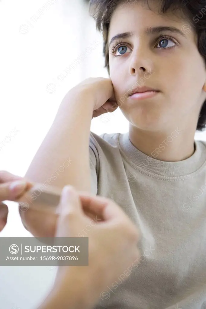 Boy having adhesive bandage applied to his elbow, cropped view
