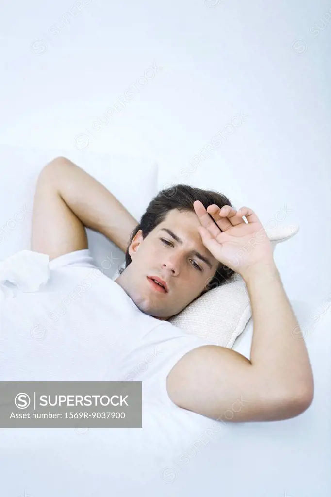 Man lying on sofa with tissue on his chest, hand on forehead