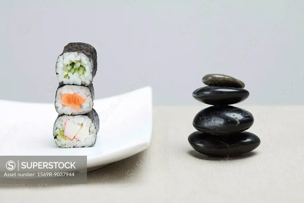 Stack of three pieces of maki sushi placed alongside stack of shiny black pebbles
