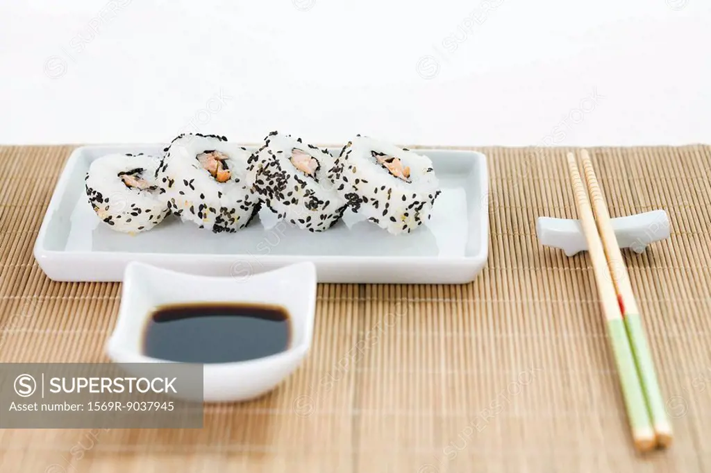Maki sushi with soy sauce and chopsticks arranged on bamboo placemat