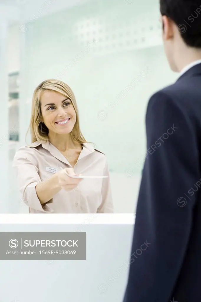 Professional woman standing behind counter, handing document to businessman