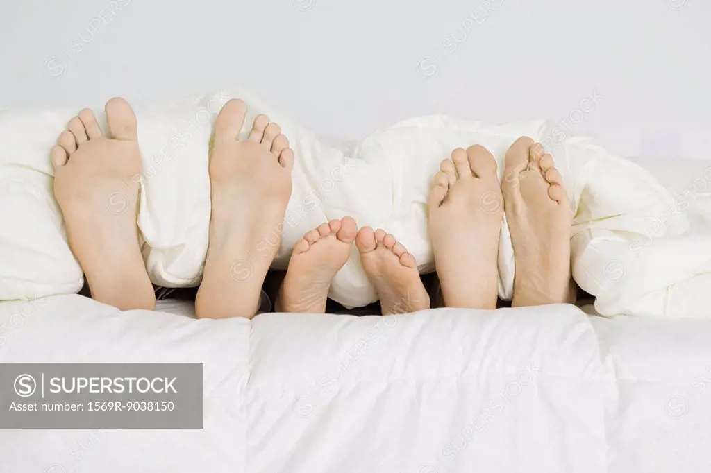 Child lying between parents under comforter, only bare feet sticking out