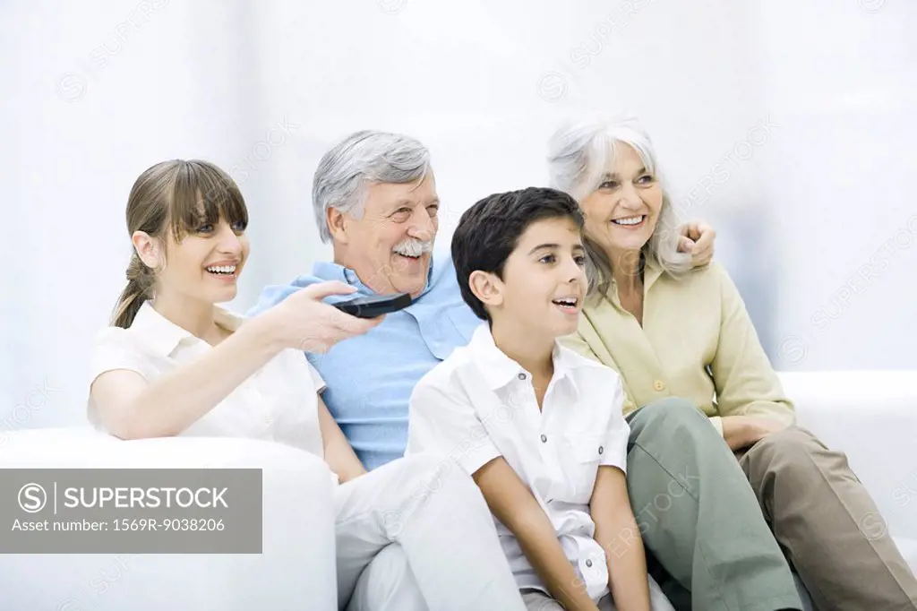 Multi-generation family sitting together on sofa, watching TV