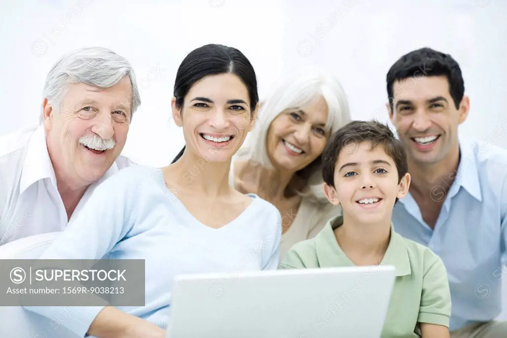 Multi-generation family gathered around laptop computer, smiling at camera
