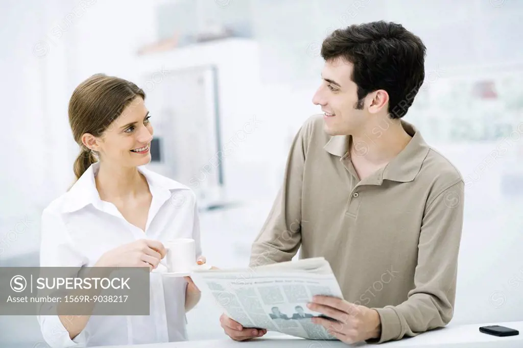 Couple smiling at each other, man holding newspaper, woman holding coffee cup