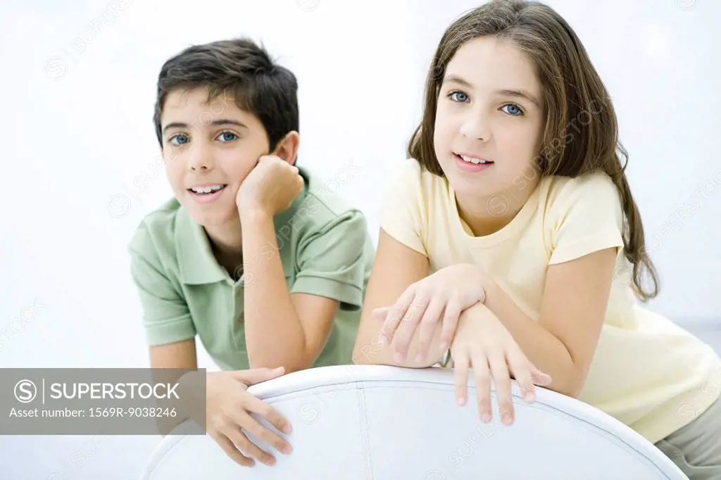 Brother and sister leaning against chair, smiling, portrait