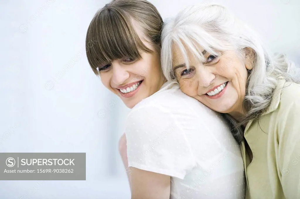 Senior woman leaning against adult daughter´s back, smiling at camera