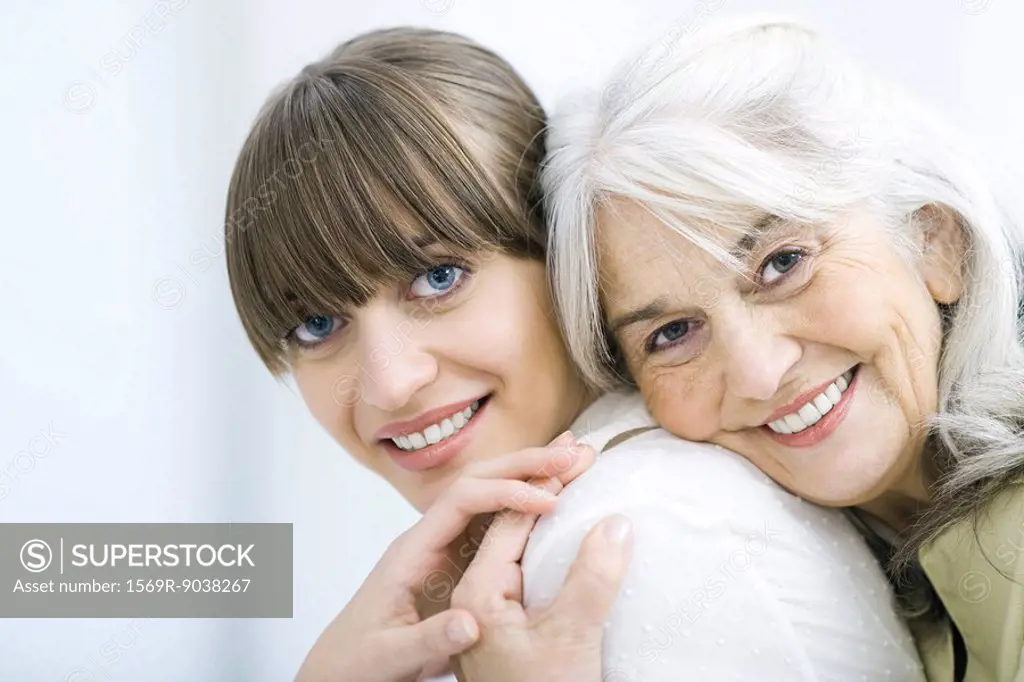 Senior woman leaning against adult daughter´s back, both smiling at camera and holding hands