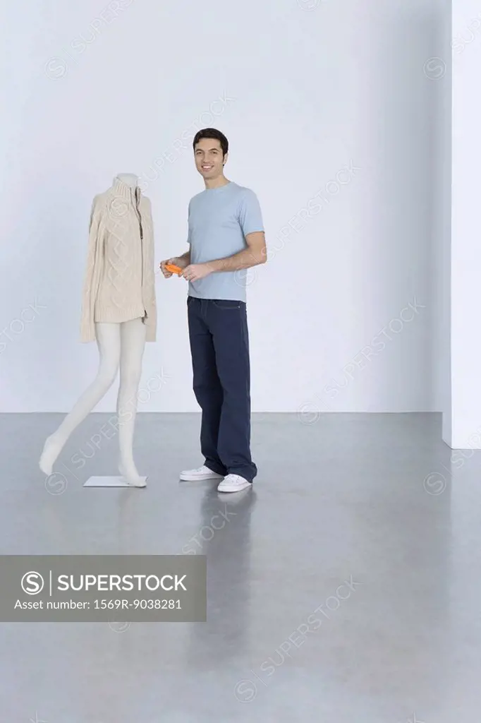 Man standing beside sweater on mannequin, holding price tag, smiling at camera