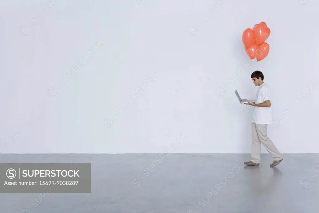 Man carrying laptop computer and heart balloons, side view
