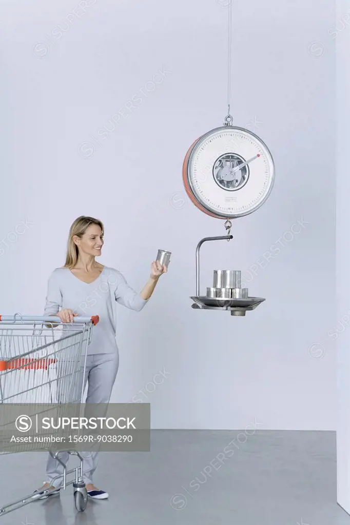 Woman standing with shopping cart, placing cans on scale