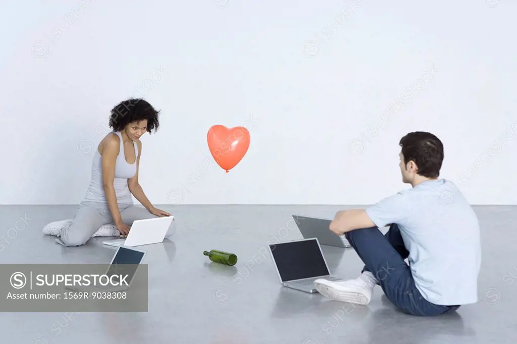Man and woman sitting with laptop computers, playing spin the bottle