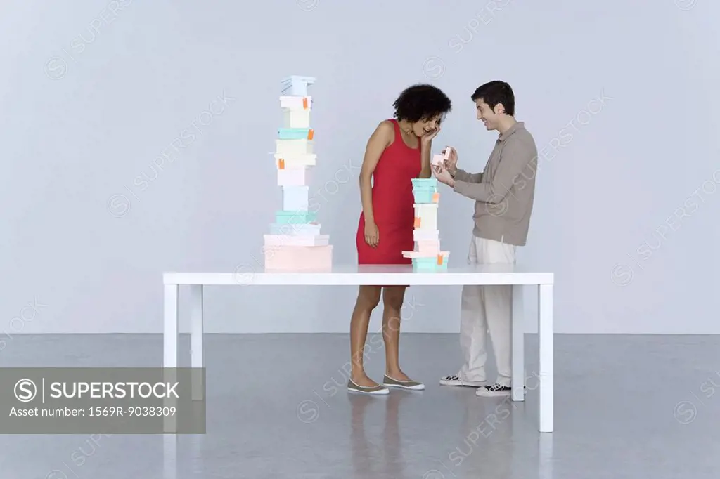 Couple standing beside table stacked with boxes, man giving woman a gift