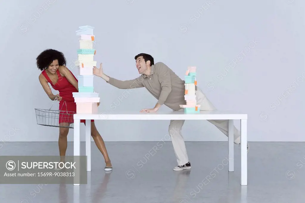 Man and woman reaching for tall stack of boxes, woman holding shopping basket
