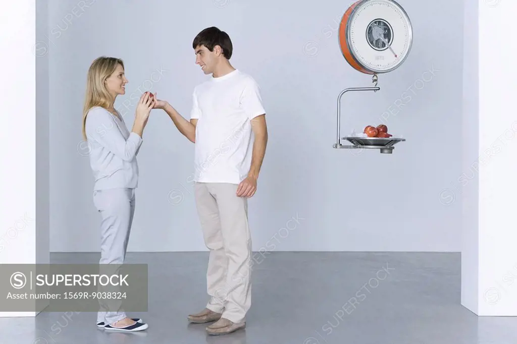 Man giving woman an apple, more apples on scale behind him