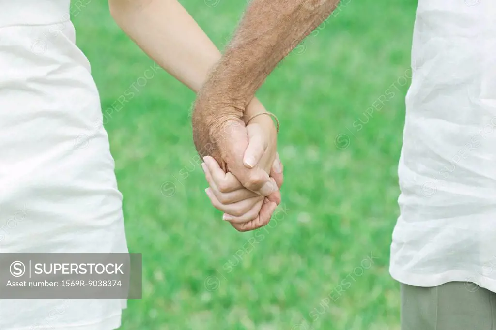 Granddaughter and grandfather holding hands outdoors, cropped view