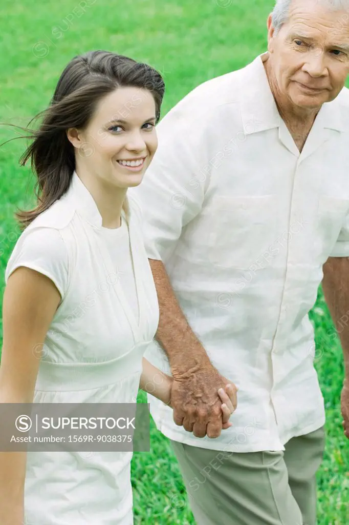 Teen girl walking hand in hand with grandfather, smiling at camera