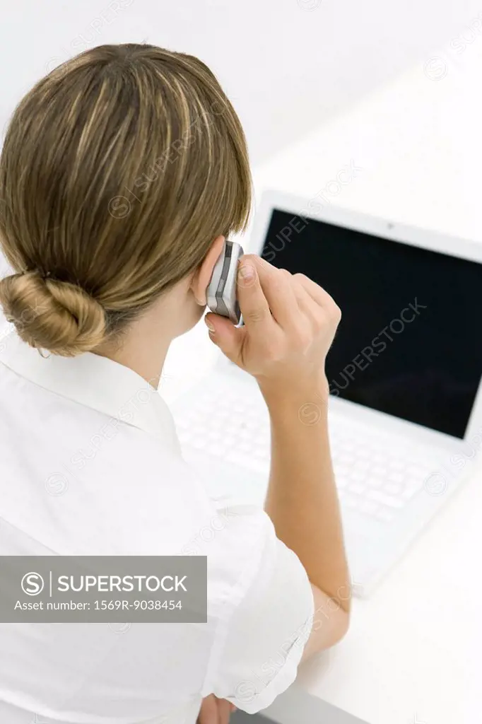 Woman using cell phone, looking at laptop, rear view